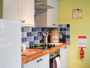 a kitchen with white cabinets and blue tiles on the wall at Little Tern in Winterton-on-Sea