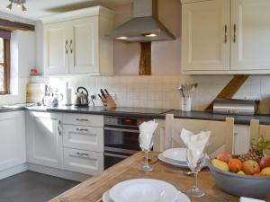 una cocina con armarios blancos y una mesa con un bol de fruta en Stocks Tree Cottage en Preston Wynne