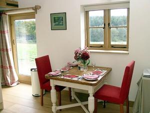 a dining room table with red chairs and a vase of flowers at Coblye Barn in Brightling