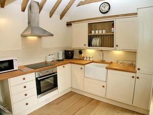 a kitchen with white cabinets and a clock on the wall at Coblye Barn in Brightling