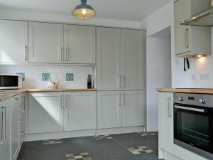 a white kitchen with white cabinets and a microwave at Loch Shore Cottage in Dornie