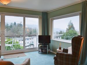 a living room with a tv and two large windows at Lake View in Bowness-on-Windermere