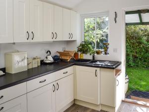 a kitchen with white cabinets and black counter tops at Woodburn Cottage in Soutergate