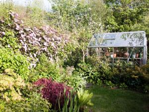 a glass greenhouse in a garden with flowers at Woodburn Cottage in Soutergate