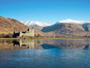 a castle in the middle of a lake with mountains at Blackmill Cottage in Taynuilt