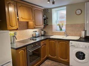 eine Küche mit Holzschränken, einer Spüle und einem Geschirrspüler in der Unterkunft Bunbury Cottage in Keswick