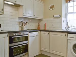 cocina con armarios blancos, fregadero y lavavajillas en Trentham Cottage, en Snettisham