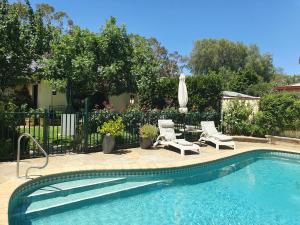 a swimming pool with two chairs and a umbrella at Courtsidecottage Bed and Breakfast in Euroa