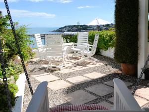 d'une terrasse avec des chaises blanches et une table donnant sur l'océan. dans l'établissement Seaside Stories, à Brixham