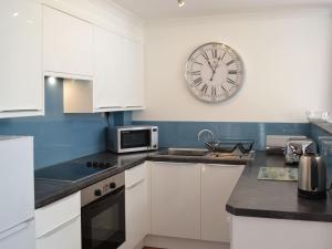 a kitchen with white cabinets and a clock on the wall at Sunny Skies in St Austell
