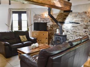 sala de estar con muebles de cuero y pared de piedra. en Oak Cottage en Woolfardisworthy