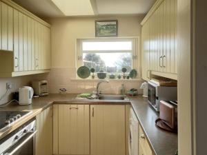 uma cozinha com armários brancos, um lavatório e uma janela em Tarandoun Cottage em Helensburgh