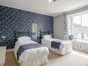 two beds in a bedroom with blue wallpaper at Holly House in Pooley Bridge