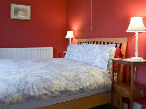 a bedroom with a bed and a red wall at Downhouse Cottage in Delabole