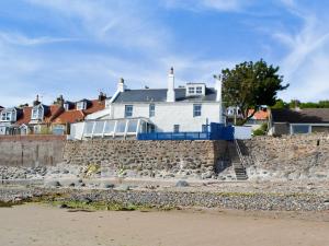a white house on a stone wall next to the beach at White Cottage in Lower Largo