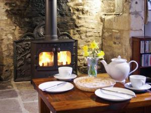a table with a wood stove with plates and cups at Ivy Cottage in Chedworth