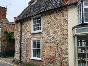 an old brick building with white windows on a street at Poppies in Blakeney