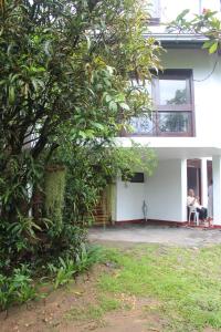 Una donna seduta su una sedia fuori da una casa bianca di Lazy Bear Best Hostel in Kandy a Kandy
