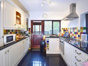 a kitchen with white cabinets and colorful tiles on the walls at South Lodge Cottage in Standish