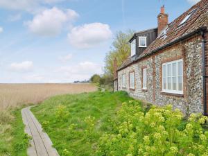 an old brick house with a path next to a field at Marsh Barn in Brancaster