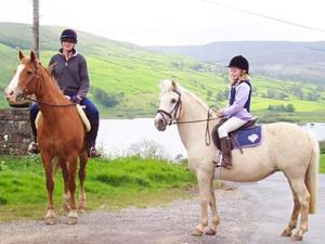 two girls are riding on horses on a road at 3 Gill Edge Cottages in Countersett