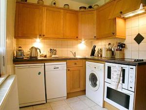 uma cozinha com armários de madeira e uma máquina de lavar e secar roupa em Glencoe Cottage em Glencoe