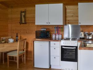 a kitchen with white appliances and a wooden wall at Birdsong Cabin in Breakish