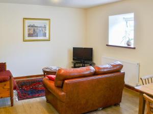 a living room with a leather couch and a television at Piglet Cottage in Elsdon