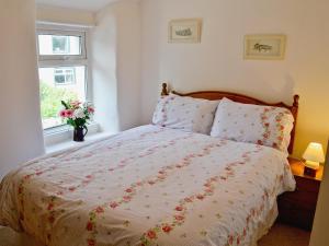 1 dormitorio con 1 cama con colcha de flores y ventana en Jackdaw Cottage, en Baycliff