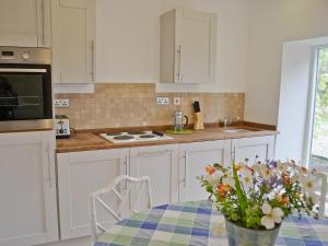 a kitchen with white cabinets and a table with a vase of flowers at The Bothy in Laverton