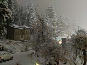 a house covered in snow with trees and a car at Sparsh Resort in Manāli