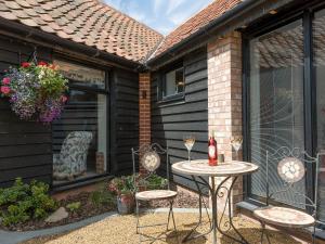 un patio con 2 sillas y una mesa con una botella de vino en The Cow Shed, en Horning