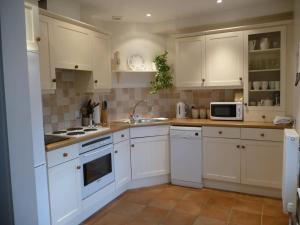 a kitchen with white cabinets and white appliances at Brook Cottage in Baltonsborough +5 photos