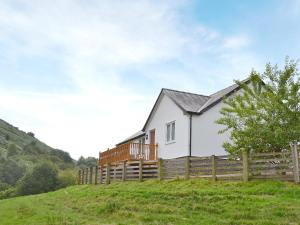 Biały dom na wzgórzu z drewnianym płotem w obiekcie Swallow Cottage w mieście Llanfair Caereinion