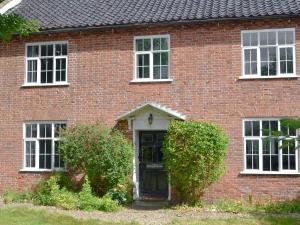 a red brick house with a black door and two bushes at The Officers House in Bacton