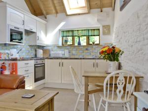cocina con armarios blancos, mesa y sillas en The Dairy en Arlingham