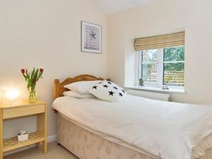 a bedroom with a large white bed and a window at Pebble Cottage in Holt