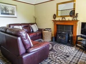 sala de estar con sofá de cuero y chimenea en Blaeberry Cottage - 28061, en Dinwoodie Mains