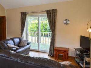 a living room with a leather couch and a sliding glass door at Black Horse Cottage in Pentraeth