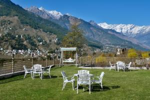 a group of tables and chairs on a field with mountains at juSTa Grand View Resort & Spa, Manali in Manāli