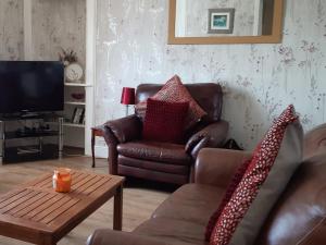 a living room with a leather couch and a coffee table at Old Barn Farm Cottage in Uplawmoor