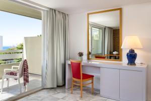 Zimmer mit einem Schreibtisch mit einem Spiegel und einem Balkon. in der Unterkunft Dionysos Hotel in Ixia