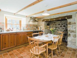 cocina con mesa, sillas y pared de piedra en Thatch Cottage, en Saint Hilary