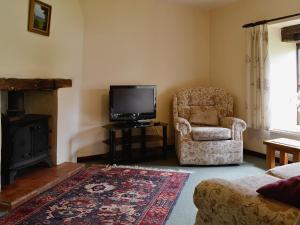 a living room with a chair and a television at Honeysuckle Cottage - 29938 in Holcombe Burnell