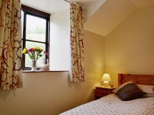 a bedroom with a bed and a window with a vase of flowers at Honeysuckle Cottage - 29938 in Holcombe Burnell