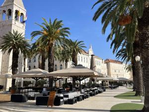 een binnenplaats met tafels, parasols en palmbomen bij MY DALMATIA - M Apartment Trogir with free parking and roof terrace in Trogir