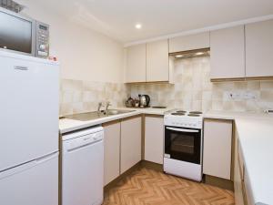 a white kitchen with white appliances and wooden floors at Grebe Cottage in Dilham