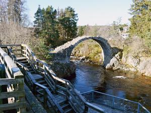 a stone arch bridge over a river with benches at Tall Pines in Carrbridge