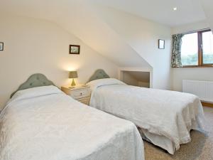 2 bedden in een zolderslaapkamer met een raam bij Coot Cottage in Dilham