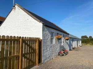 a white brick building with a wooden fence and flowers at Pleacairn Cottage in Dalton